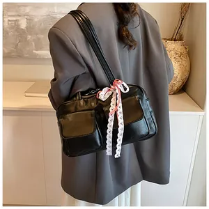 Detail of black glossy shoulder bag with twin front pockets and decorative lace bow