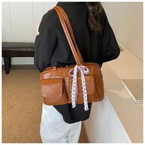Detail of caramel brown tote bag with twin front pockets and white lace bow on the handle