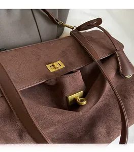 Dettaglio della borsa a spalla in camoscio marrone con chiusura girevole dorata e texture morbida