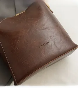 Detail der dunkelbraunen geflochtenen Ledertasche mit goldenem Logo und strukturierter Optik