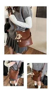 Detail der braunen Eimer-Tasche mit geflochtenem Griff, Metallstab und Löwen-Anhänger