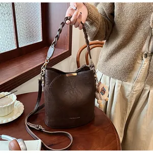 Detailansicht braune Eimertasche mit Webgriff und Löwenanhänger im gemütlichen Café