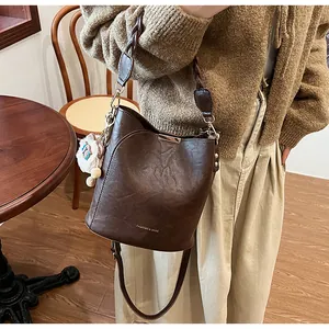 Details einer dunkelbraunen Eimer-Tasche mit geflochtenem Griff und Plüsch-Anhänger