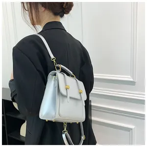 Détail d'un sac à dos bleu clair en cuir poli porté sur un blazer noir avec boucles d'or