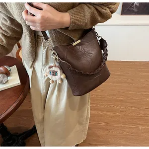 Detail einer braunen Eimertasche mit geflochtenem Griff und süßem Plüsch-Schafanhänger