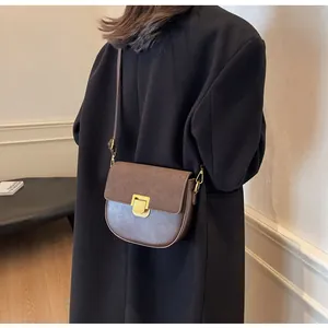 Borsa a sella in pelle marrone con fibbia dorata su modella con cappotto nero