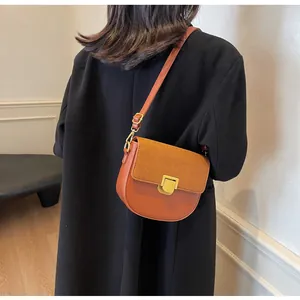 Borsa a sella marrone vista laterale su modella con cappotto nero e tracolla