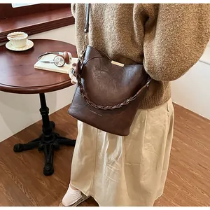 Dunkelbraune Beuteltasche mit Goldakzenten und Flechtgriff in gemütlicher Café-Szene