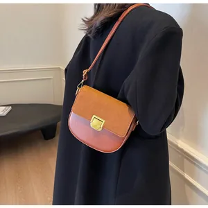 Dettaglio borsa a sella marrone bicolore con fibbia dorata indossata su un cappotto nero