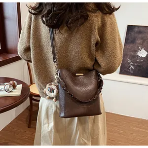 Detail der dunkelbraunen Beuteltasche mit geflochtener Kette und Bärenanhänger