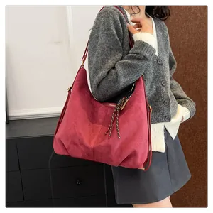 Detail of burgundy faux suede shoulder bag featuring a woven tassel pendant and zip closure