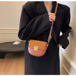 Dettaglio borsa a sella marrone con patta in pelle scamosciata e fibbia d'oro su cappotto