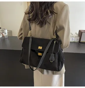 Dettaglio della borsa a spalla in camoscio nero con doppia chiusura dorata su blazer