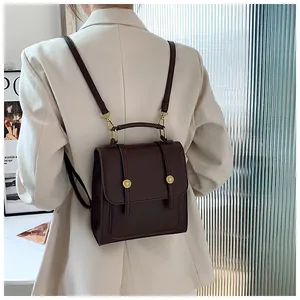 Détail d'un sac à dos en cuir marron foncé avec boucles dorées sur un blazer crème