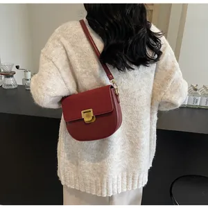 Dettaglio borsa a sella in pelle rosso scuro con fibbia dorata indossata da modella