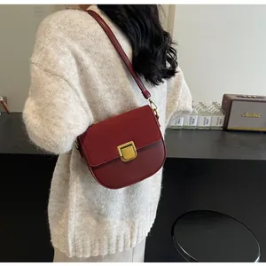Dettaglio borsa a sella rosso-marrone con fibbia dorata vintage su maglione crema