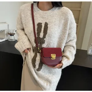Dettaglio borsa a sella bordeaux con patta in pelle scamosciata e chiusura dorata