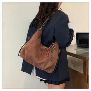Brown suede hobo bag with braided zipper detail shown in a minimalist office setting