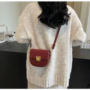 Dettaglio della borsa a sella bordeaux con patta in pelle scamosciata e fibbia d'oro