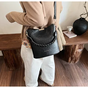 Detail einer schwarzen Beuteltasche mit Flechtgriff und Bärenanhänger auf einer Bank