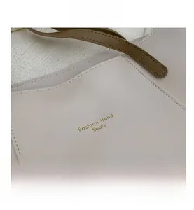 Close-up of cream leather tote bag with gold stamped logo and dark brown shoulder strap