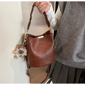Detail der braunen Eimer-Tasche mit geflochtenem Griff und süßem Plüschschaf-Anhänger