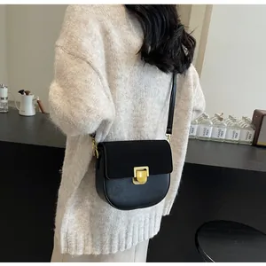Dettaglio borsa a sella nera con fibbia dorata indossata su un maglione panna
