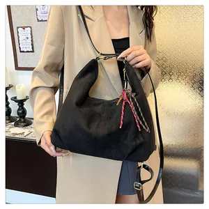 Detailed view of black suede hobo bag with red woven rope knot and golden key pendant