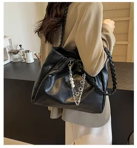 Detail of black pebbled faux leather tote with woven shoulder strap and silver chain