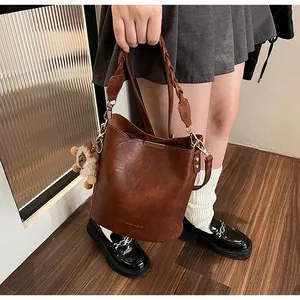 Detail der dunkelbraunen Eimer-Tasche mit gewebtem Griff und Löwen-Plüschanhänger
