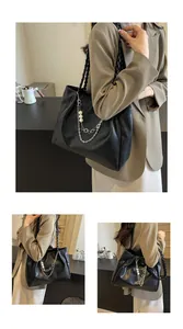 Close-up of black leather tote with silver chain, white pearls and woven shoulder strap