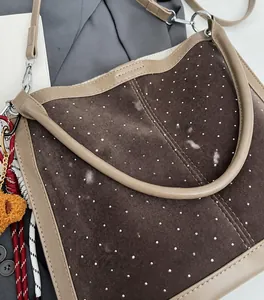 Detail of dark brown suede bag featuring silver rivets and plush bear pendant detail