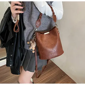 Detailansicht einer braunen Beuteltasche mit geflochtenem Griff und Plüschanhänger-Deko