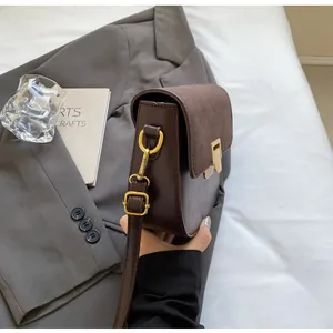 Dettaglio borsa a sella in pelle marrone scuro con fibbia dorata e cuciture a contrasto