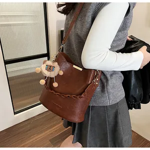 Detail der braunen Leder-Eimertasche mit geflochtenem Griff und Plüschtier am Modell