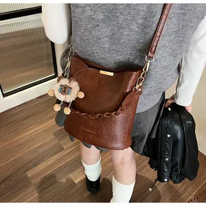 Detail der braunen Vintage-Eimertasche mit geflochtenem Griff und Löwen-Plüschanhänger