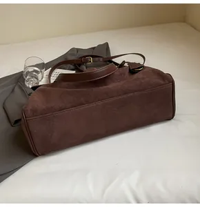 Dettaglio della texture scamosciata marrone e del manico in pelle di una borsa a tracolla