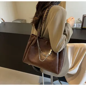 Detail of deep brown tote bag with woven strap, silver chain, and pearl accents
