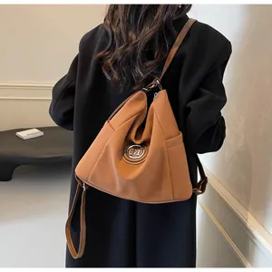 Detailansicht einer kamelfarbenen Hobo-Tasche mit M-Logo an einem Model im schwarzen Mantel