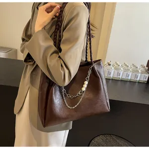 Detail of dark brown tote bag featuring braided straps and a pearl floral chain accent