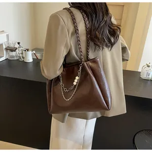 Detail of dark brown tote bag with woven handle, metal chain and pearl accents
