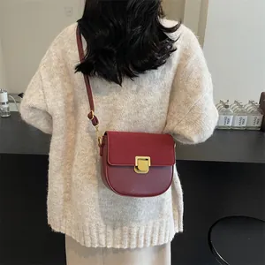 Borsa a sella in pelle e scamosciato rosso scuro con fibbia dorata su maglia beige