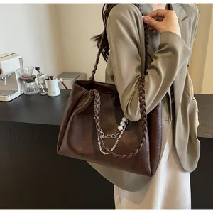 Detail view of deep brown tote bag featuring elegant pearl chain and braided strap
