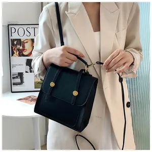Gros plan d'un sac bandoulière noir avec boucles dorées porté par un mannequin en tailleur