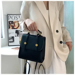 Détail d'un sac à dos vintage noir avec boucles dorées porté avec un blazer blanc