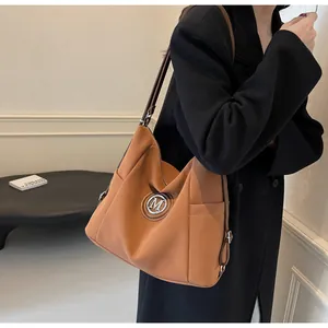 Detail der braunen Ledertasche mit silbernem M-Logo und schlankem Seitentaschendesign