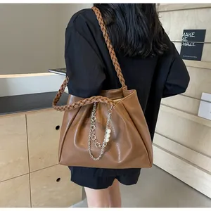 Detail of brown large tote bag with woven shoulder strap and pearl metal chain pendant