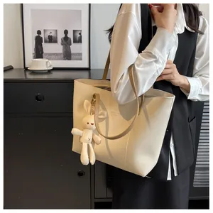 Detail of cream tote bag with thin shoulder straps and a cute beige bunny pendant charm