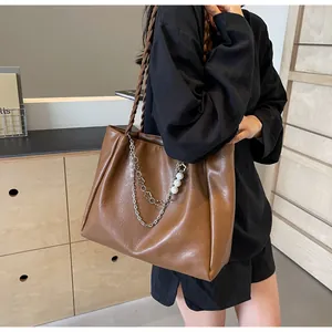 Detail of caramel leather tote bag with braided handle, metal chains and pearl charms