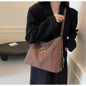 Details einer braunen Nylon-Tragetasche mit M-Logo aus Silber und Leder-Schultergurt